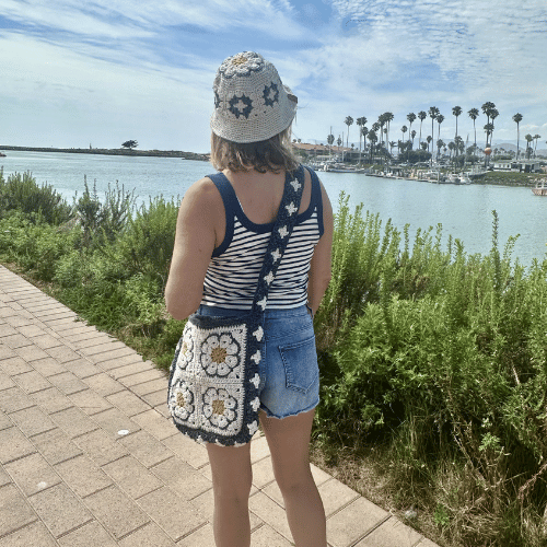A woman wearing a crochet granny square bucket hat and carrying a crochet grannt square crossbody bag